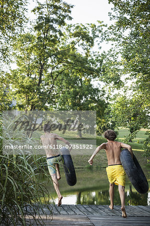 Two boys, leaping from the jetty into the water holding swim floats.