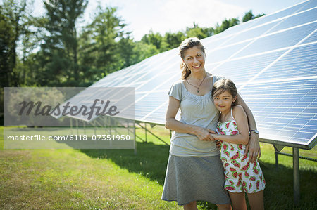 A child and her mother in the fresh open air, beside solar panels on a sunny day at a farm in New York State, USA.