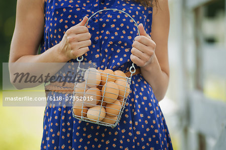 A woman holding a basket of hen's eggs gathered from the chickens on a farm.