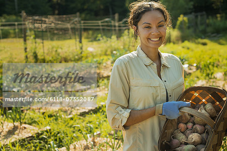 A woman carrying a basket of freshly gathered vegetables and root crops.
