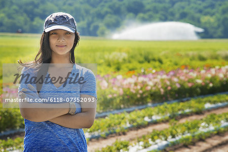 A woman with arms folded, standing in a field, full of fresh salad and vegetable crops and flowers.