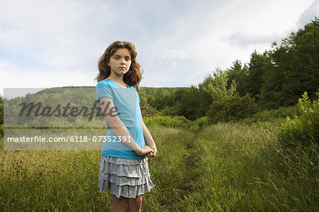 A young girl standing by a path through the long grass in a field.