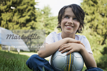 A boy holding a football, sitting on the grass. Solar panels.