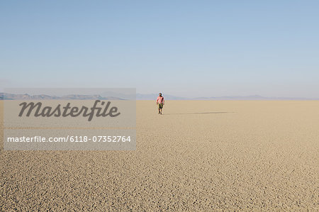 Man walking across a flat desert landscape