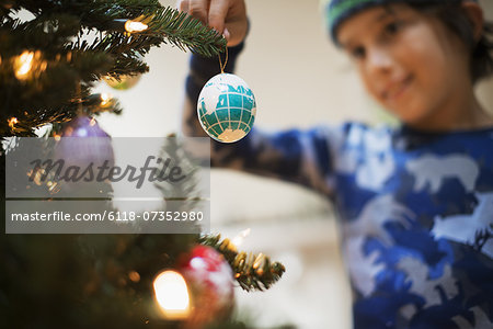 A young boy holding Christmas ornaments and placing them on the Christmas tree.