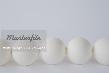 End-on view of free range, organic eggs with white shells arranged in a row, on a white background.