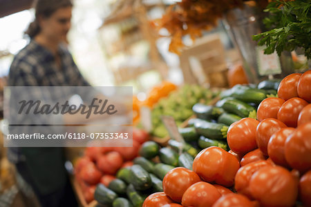 Organic Farmer at Work. A young man arranging a display of fresh produce on a farm stand, tomatoes and cucumbers.