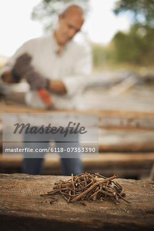 A man working in a reclaimed timber yard. Using a tool to remove metals from a reclaimed piece of timber. A heap of rusty metal nails. A man working in a reclaimed timber yard. Using a tool to remove metals from a reclaimed piece of timber. A heap of rusty metal nails.