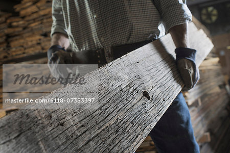 A heap of recycled reclaimed timber planks of wood. Environmentally responsible reclamation in a timber yard. A man carrying a large plank of mature weathered wood.