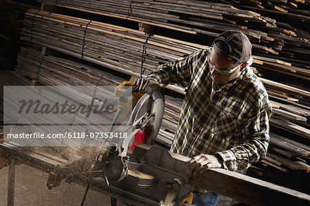 A reclaimed lumber workshop. A man in protective eye goggles using a circular saw to cut timber.