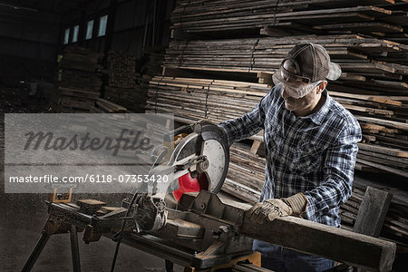 A reclaimed lumber workshop. A man in protective eye goggles using a circular saw to cut timber.