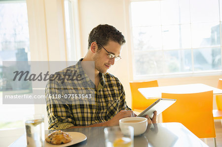 A young man in a coffee shop reading using a tablet computer.