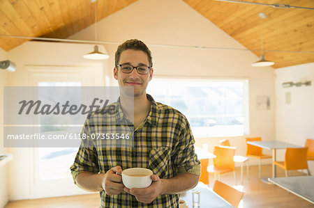A young man standing holding a cup of coffee in a coffee shop.