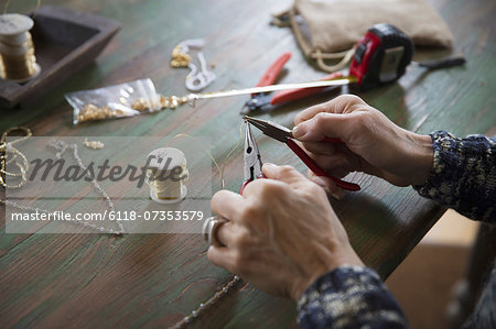 A tabletop with jewellery making equipment. Hands twisting wire on a necklace.
