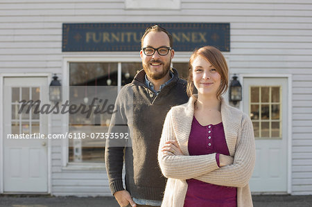 A man and woman standing outside a storefront on a street. A couple running an antique shop.