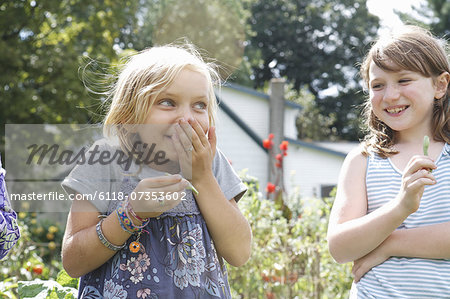 Two children standing outdoors in a garden laughing.