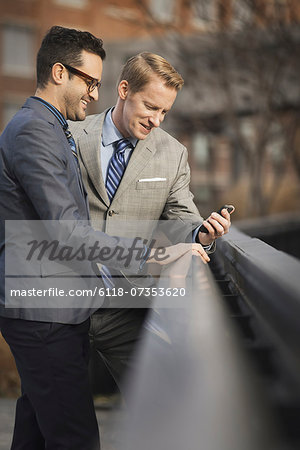 Two men in formal business clothes, standing side by side, looking at a cell phone screen or mobile phone.