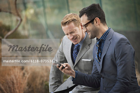 Two men in formal business clothes, standing side by side, looking at a cell phone screen or mobile phone.