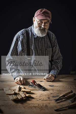 A man working in a reclaimed lumber yard workshop. Holding tools and working on a knotted and uneven piece of wood.