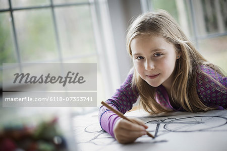 A family home.  A child sitting at a table using a pencil and creating a line drawing. Artwork. Drawing.