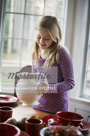 Children in a family home.  A girl  holding a white pottery jug. Table laid with crockery.