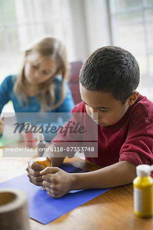 Children in a family home.  Two children sitting at the table, using paint and paper to create decorations.