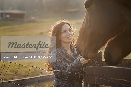 A woman stroking the muzzles of two horses in a paddock on an organic farm.