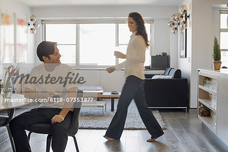 Couple at Home, Man using smartphone, Woman walking past