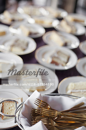 A table laden with plates. White china, and a basket full of dessert forks. A slice of wedding cake. A table laden with plates. White china, and a basket full of dessert forks. A slice of wedding cake.
