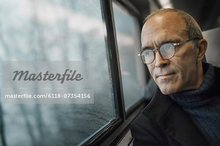 A mature man sitting in a window seat on a train journey, looking out into the distance.