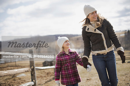 A woman and child walking along a path hand in hand on a farm in spring weather.