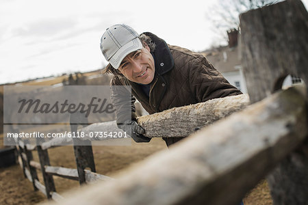 A man leaning against a post and rail fence on a farm in winter.