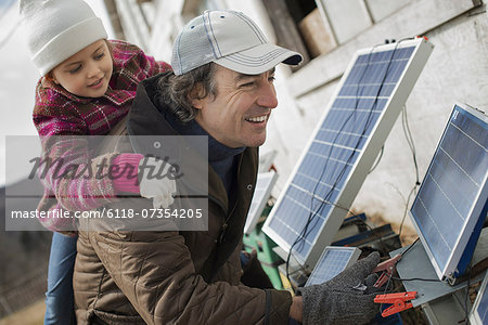 A man giving a child a piggybank while trying to connect the leads for solar power panels.