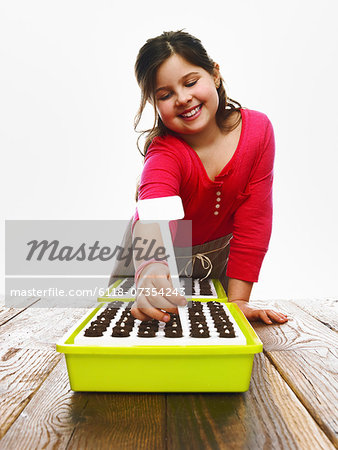 A young girl planting seeds in a modular seed tray with dark organic soil.