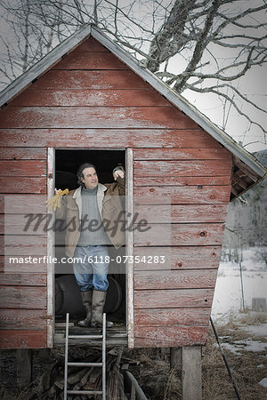 An organic farm in upstate New York, in winter. A man standing in the doorway of a henhouse.