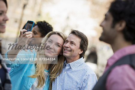 People outdoors in the city in spring time. A woman using her cell phone to take a photograph. A group of friends, men and women.