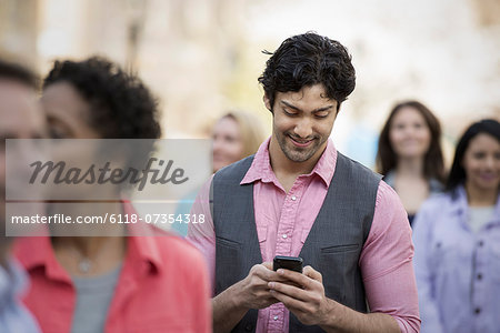 People outdoors in the city in spring time. A group of men and women. A man looking at his cell phone.