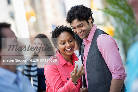 People outdoors in the city in spring time. New York City park. Four people, men and women. A couple looking at a mobile phone screen.