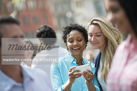People outdoors in the city in spring time. New York City. A group of men and women, two women looking at a cell phone. People outdoors in the city in spring time. New York City. A group of men and women, two women looking at a cell phone.