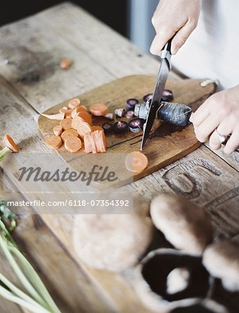 A domestic kitchen tabletop. A person chopping fresh vegetables on a chopping board with a knife.