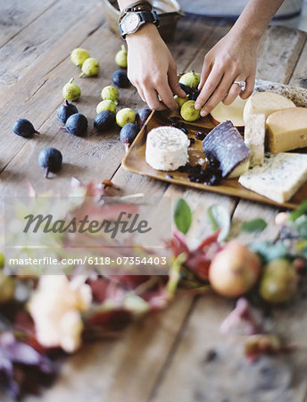 A woman at a domestic kitchen table. Arranging fresh fruit, black and green figs on a cheese board. Organic food. From farm to plate.