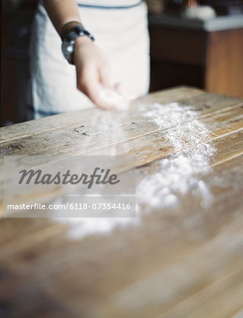 A domestic kitchen. A woman cooking. Spreading flour across a tabletop.