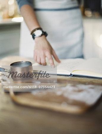 A woman in a domestic kitchen, reading a recipe book.