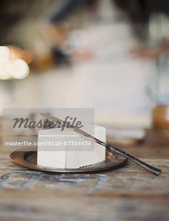 A domestic kitchen. A woman in the background. A slab of fresh organic butter, on a wooden dish. A domestic kitchen. A woman in the background. A slab of fresh organic butter, on a wooden dish.