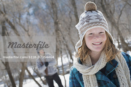 Winter scenery with snow on the ground. A young girl with a bobble hat and scarf outdoors. A man in the background.