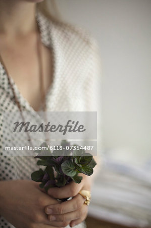 A woman wearing a dress and necklace, holding a small bunch of red and green plant leaves. Cologne mint leaves.