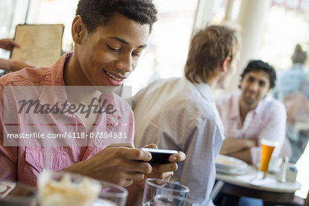 Urban Lifestyle. Three young men in a cafe. One checking his smart phone. Two talking at a table.