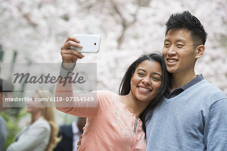 City life in spring. Young people outdoors in a city park. A couple taking a self portrait or selfy with a smart phone.