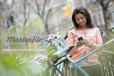 City life in spring. A young woman in a peach coloured shirt, using her smart phone. Bicycles parked in a bike rack.