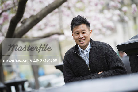 City life in spring. A young man outdoors in a city park. Sitting on a bench.